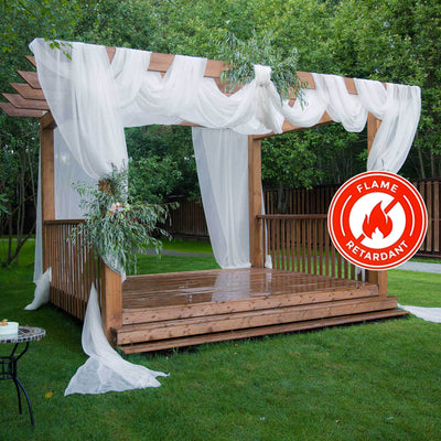 Flame retardant wooden pergola with sheer drapes and greenery in a garden setting.