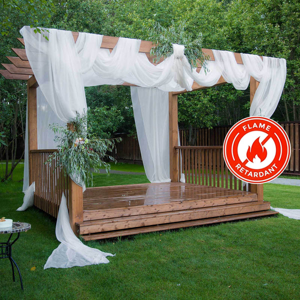 Flame retardant wooden pergola with sheer drapes and greenery in a garden setting.