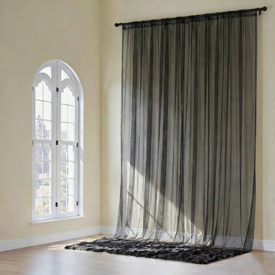 Sheer black curtain draped elegantly in a bright room with an arched window.