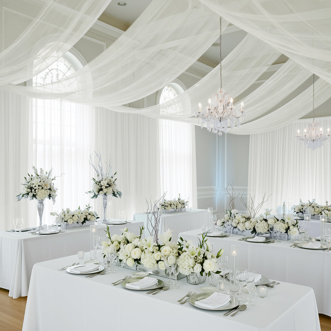 Elegant white wedding reception with floral arrangements and draped fabric decor.