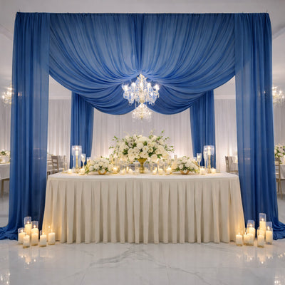 Elegant wedding reception setup with blue drapes, floral arrangements, and candles.