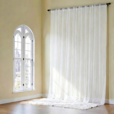 Sheer white curtains hanging in a bright room with arched window.