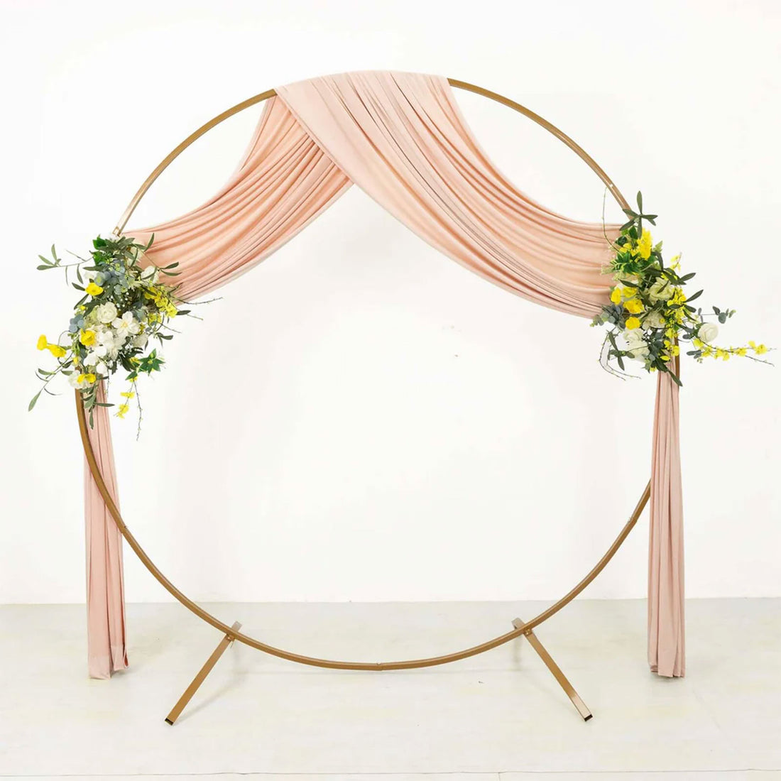 Round wedding arch with blush drapes and floral arrangements on gold frame