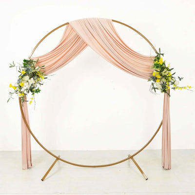 Round wedding arch with blush drapes and floral arrangements on gold frame