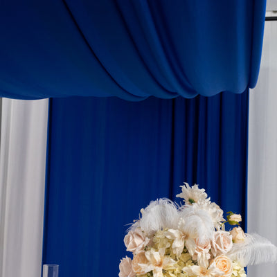 Elegant floral arrangement with feathers under blue drapery.