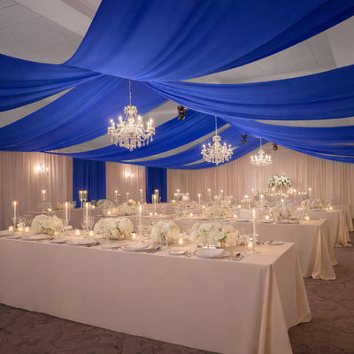 Elegant wedding reception setup with blue drapes and white floral centerpieces.