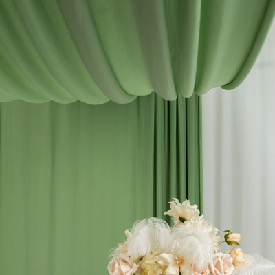 Green draped fabric backdrop with floral arrangement in the foreground.