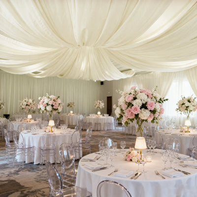 Elegant wedding reception setup with floral centerpieces and draped ceiling.