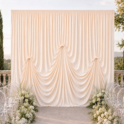 Elegant outdoor wedding backdrop with draped ivory curtains and floral arrangements