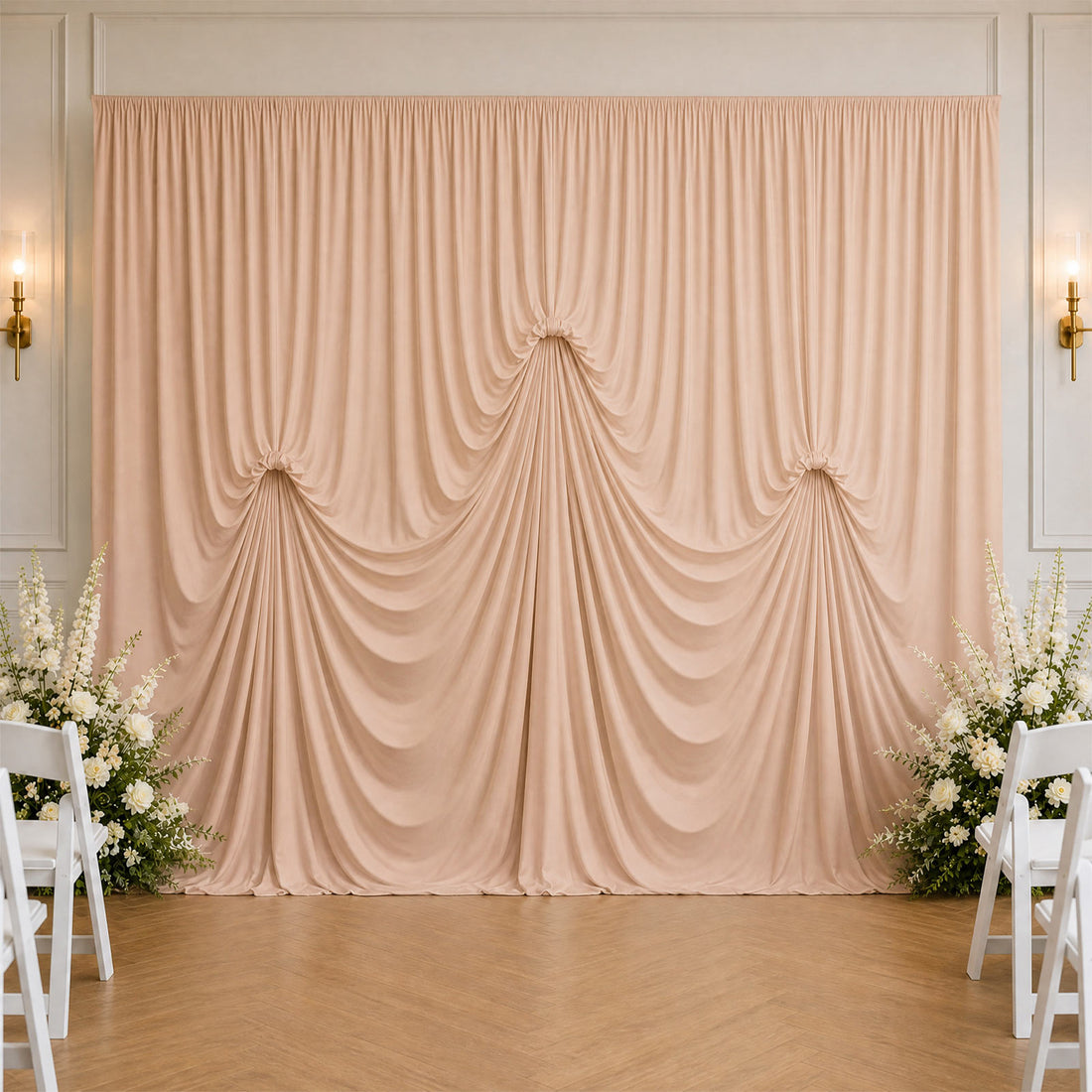 Elegant blush draped wedding backdrop with white floral arrangements and chairs