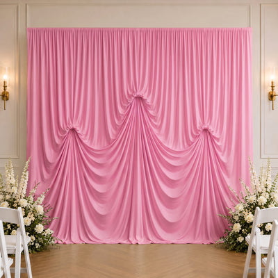 Pink draped wedding backdrop with floral arrangements and white chairs