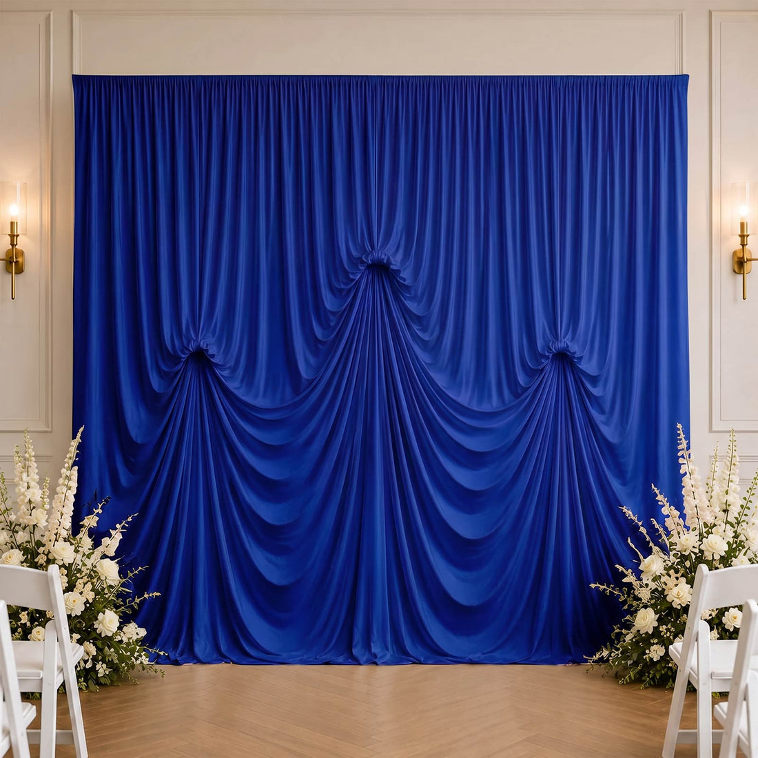 Royal blue draped wedding backdrop with white floral arrangements and chairs