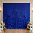 Royal blue draped wedding backdrop with white floral arrangements and chairs