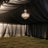 Elegant chandelier hanging in a draped black tent with grass floor.