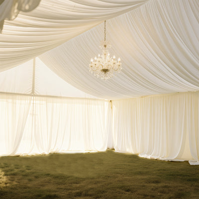 Elegant chandelier hanging in a draped tent interior with soft lighting.