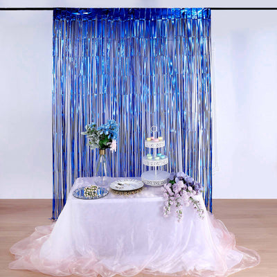 Decorative party table with flowers, cake stand, and tableware against shiny blue backdrop.