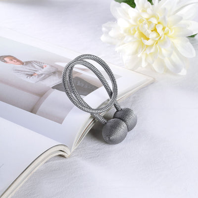 Stylish gray fabric hair tie with decorative balls on a magazine.