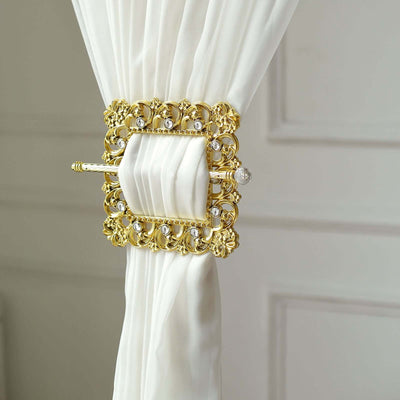 Gold decorative curtain tieback with crystal accents on white fabric.