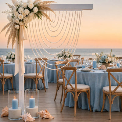 Elegant beach wedding reception with blue linens, pearls, and floral arch at sunset