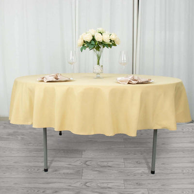 Round yellow tablecloth on a dining table with floral centerpiece and glasses.