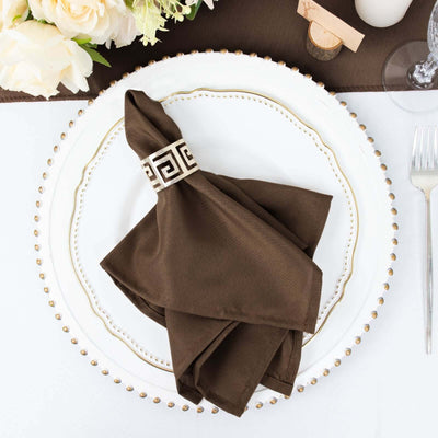 Brown napkin with decorative ring on an elegant plate setting.