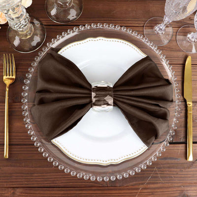 Elegant brown napkin with crystal ring on a decorative plate.