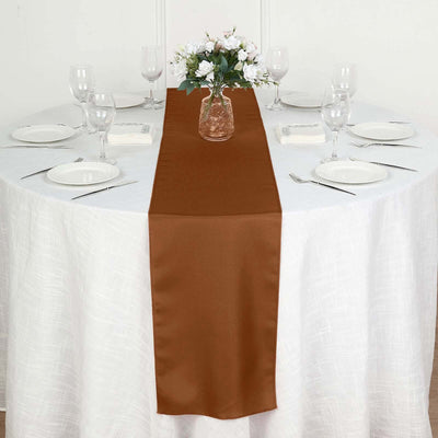 Brown satin table runner on a round table set for a meal.