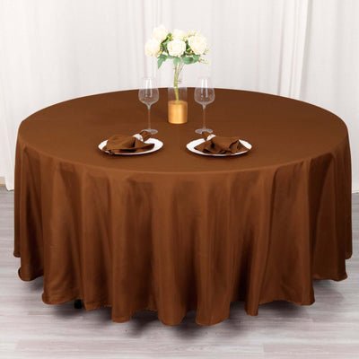 Brown round tablecloth draped over a table set for two with flowers.