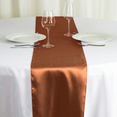 Brown satin table runner on a white table setting with glassware and plates.