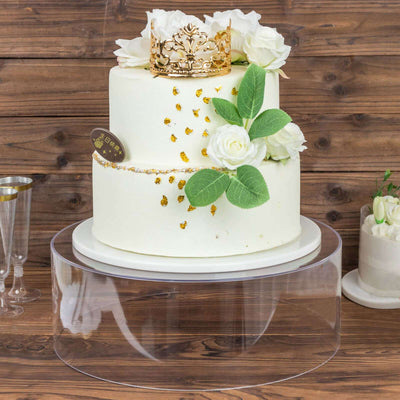 Elegant three-tier cake adorned with flowers and a crown on a clear stand.
