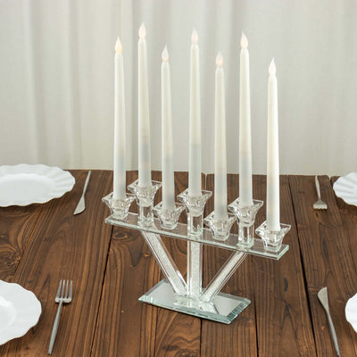 Crystal candlestick holder with seven white candles on a wooden table.