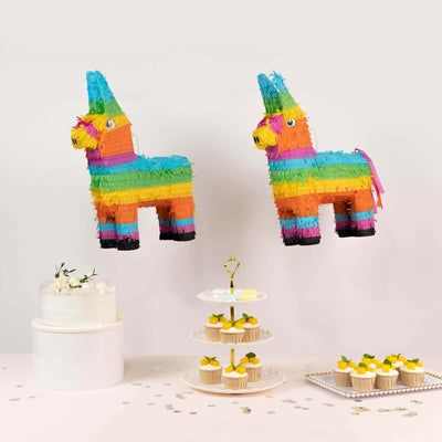 Colorful piñatas with cupcakes and a cake on a white table