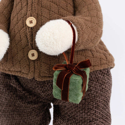 Child in brown knit winter outfit holding a green gift with white mittens