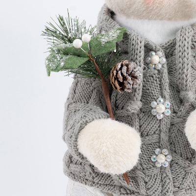 Child in gray knit winter coat holding a festive pinecone and evergreen branch