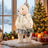Christmas teddy bear in winter outfit beside decorated tree and gifts