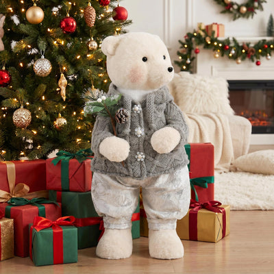 Christmas teddy bear in gray sweater beside decorated tree and gifts
