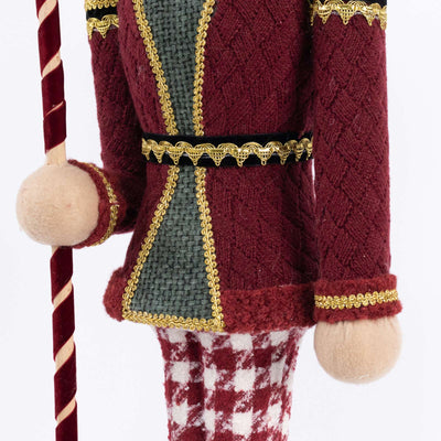 Festive nutcracker figurine in burgundy coat holding candy cane staff