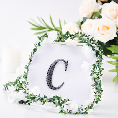 Decorative letter "C" with floral arrangement backdrop.