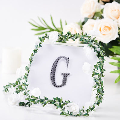 Decorative letter "G" with floral accents in a clear frame.