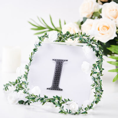 Decorative letter "I" surrounded by flowers and greenery on a white backdrop.