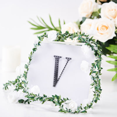 Decorative letter "V" surrounded by floral wreath and greenery.