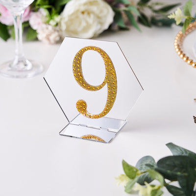 Gold glitter table number 9 in a hexagon shape on a decorative table setting.