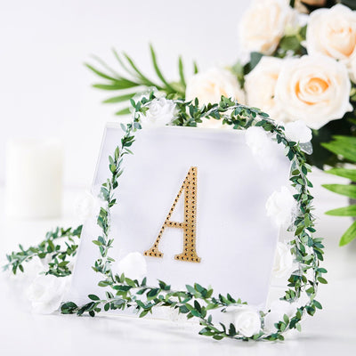 Gold letter "A" in a decorative frame with white flowers and greenery.