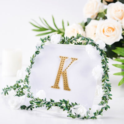 Gold letter "K" decoration with floral accents on a clear background.