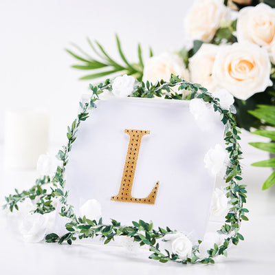 Gold letter "L" decor surrounded by faux flowers and greenery.
