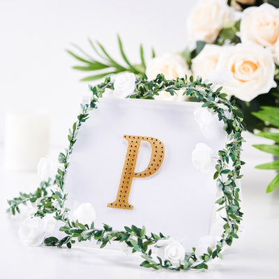 Gold letter "P" surrounded by greenery and white roses on a clear backdrop.