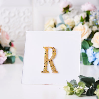 Gold glitter letter "R" on a clear display with floral background.