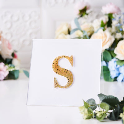 Gold rhinestone letter "S" on a white card with floral background.