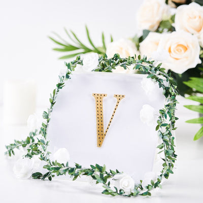 Gold letter "V" adorned with greenery and roses on a clear background.