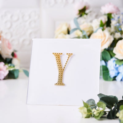 Gold rhinestone letter Y on a white display with flowers in the background.